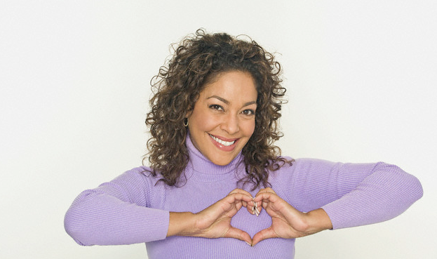 african american woman wearing a purple turtleneck making a heart symbol with the hands over her heart