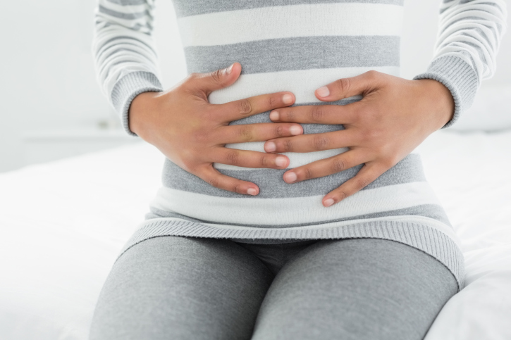 Mid section of a woman with stomach pain sitting in bed