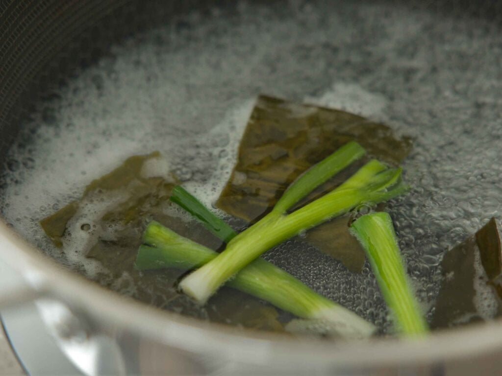15-Minute EASY Vegan Tteokbokki - Spicy Korean Rice Cakes. 7 Scallions and dashima in pot of boiling water
