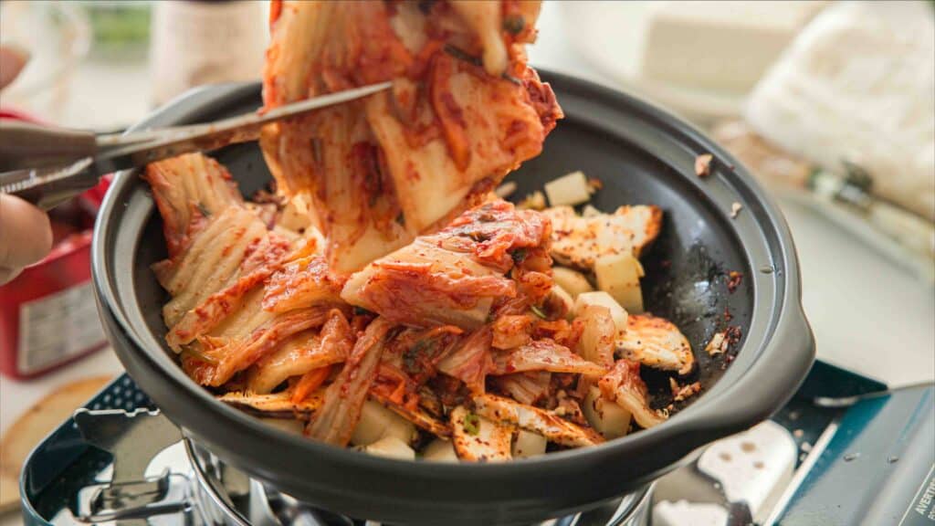 Easy & Hi-Protein Vegan Kimchi Jjigae Reigns Supreme. 13 Cutting kimchi into pot of sauteed vegetables