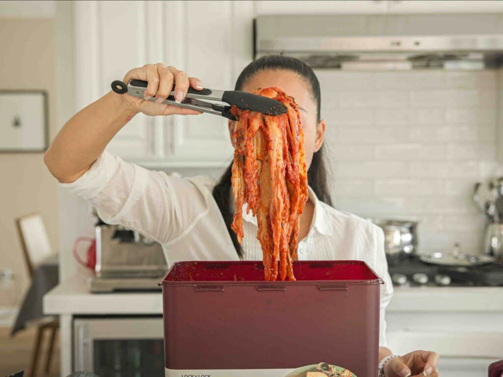 Easy & Hi-Protein Vegan Kimchi Jjigae Reigns Supreme. 3 Pulling kimchi out of kimchi container with tongs