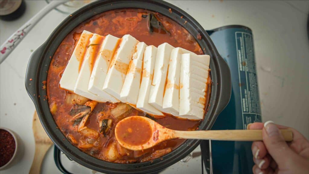 Easy & Hi-Protein Vegan Kimchi Jjigae Reigns Supreme. 4 Tofu slices added to pot of boiling vegan kimchi jjigae