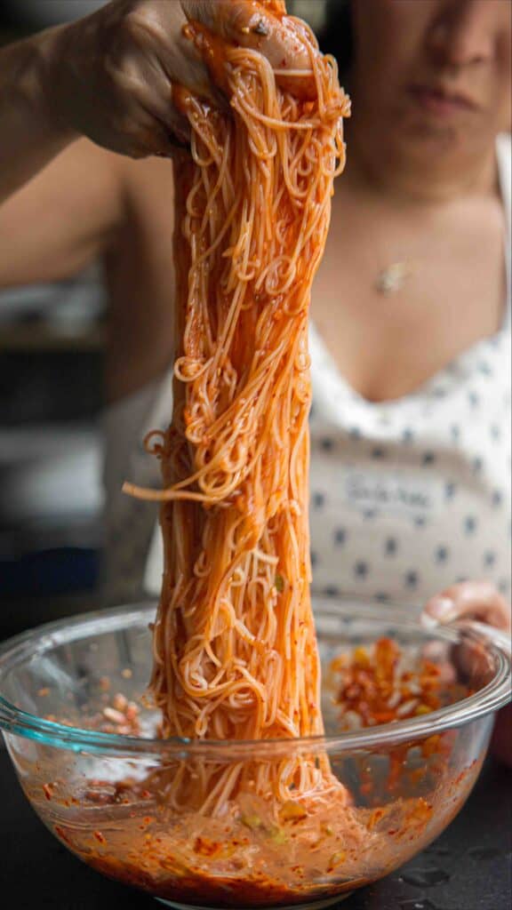 15-Minute Spicy & Cold Bibim Kimchi Noodles Recipe. 13 pulling kimchi noodles out of bowl to serve