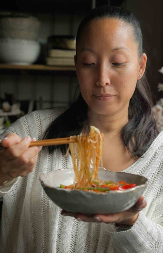 Healthy And Easy Vegan Japchae (Korean Glass Noodles). 9 woman using chopsticks to eat vegan japchae