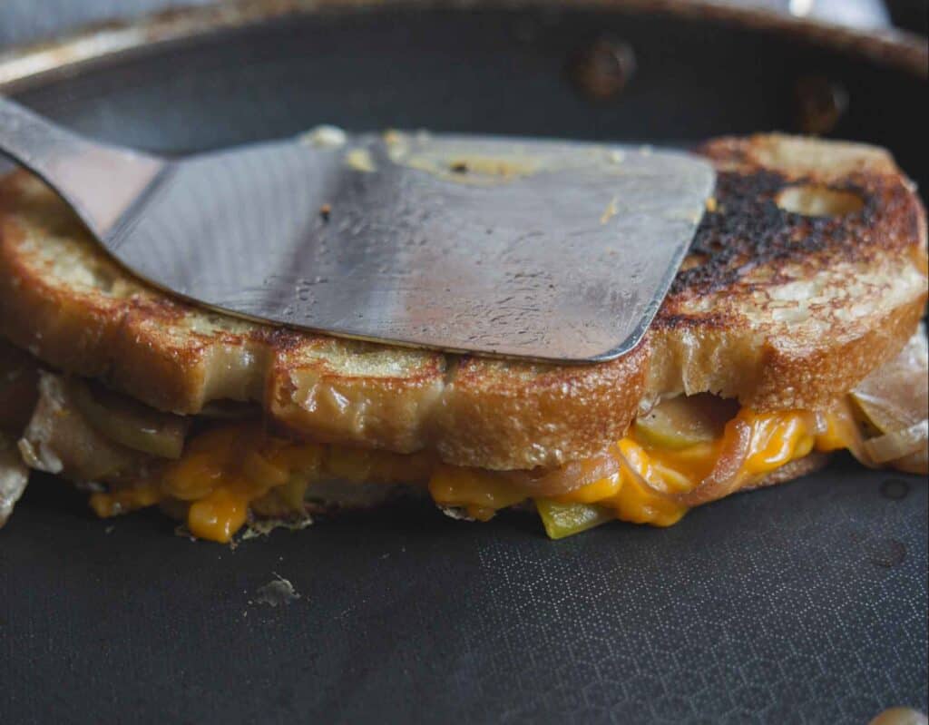The BEST Apple Cheddar Vegan Grilled Cheese Sandwich. 2 pressing spatula down on top of vegan grilled cheese sandwich