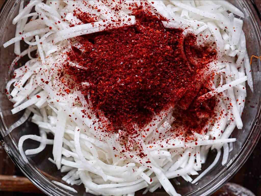 Easy & Spicy Korean Radish Salad - Musaengchae Recipe. 5 bowl of julienned radish after adding gochugaru