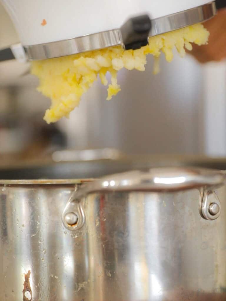 Tips on Making the BEST Creamy Mashed Potatoes (Dairy Free Option)! 5 potatoes coming out of bottom of food mill
