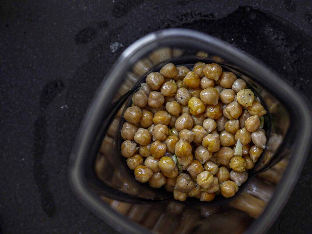 5-Ingredient Easy Chickpea Pasta Recipe (Pasta e Ceci). 10 A top view of chickpeas inside a blender jar on a dark surface. The chickpeas are light brown, some glistening with moisture, and are ready for blending.