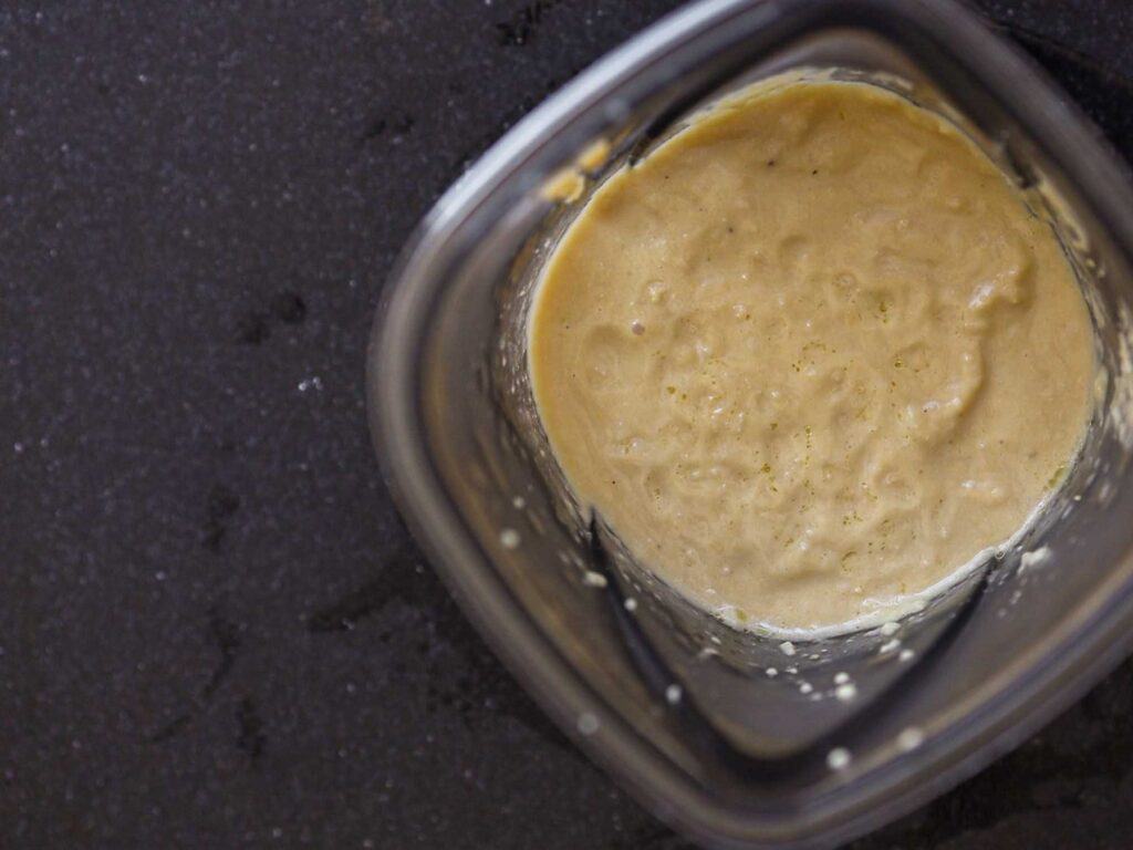 5-Ingredient Easy Chickpea Pasta Recipe (Pasta e Ceci). 13 A top-down view of a blender containing smooth, creamy chickpea sauce. The background is a dark, textured surface, highlighting the contrasting pale color of the hummus inside the blender.