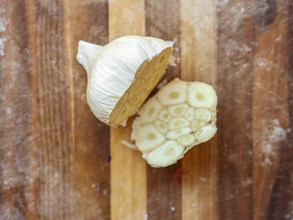 Gochujang and Roasted Carrot Soup - SPICY AND EASY. 7 A halved garlic bulb on a wooden cutting board, showing the cross-section with multiple cloves. The garlics layers and cloves are visible, surrounded by a dusting of flour on the board.