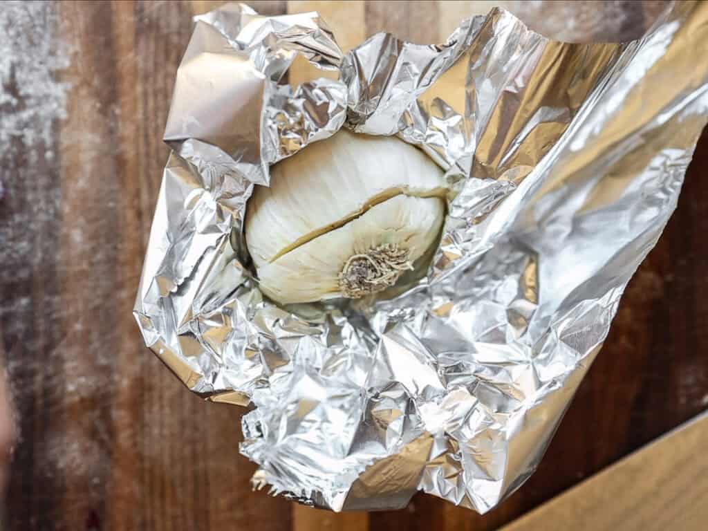 Gochujang and Roasted Carrot Soup - SPICY AND EASY. 8 A bulb of garlic partially wrapped in crinkled aluminum foil, resting on a wooden surface.