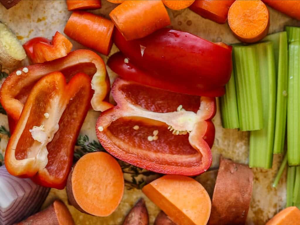 Gochujang and Roasted Carrot Soup - SPICY AND EASY. 2 A colorful assortment of chopped vegetables, including red bell peppers, carrots, celery, and sweet potatoes, displayed on a wooden surface.