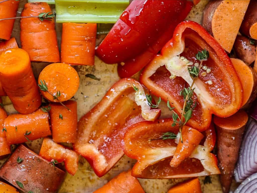 Gochujang and Roasted Carrot Soup - SPICY AND EASY. 5 Chopped vegetables including sliced carrots, red bell peppers, and sweet potatoes are seasoned with herbs on a tray, ready for roasting.