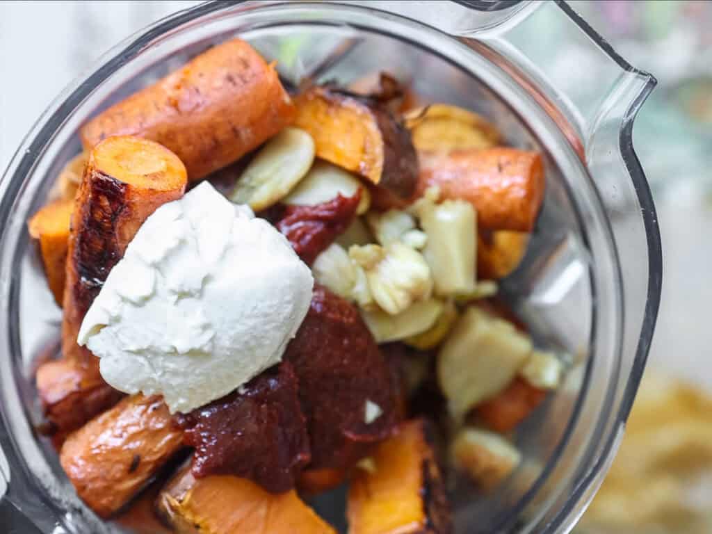 Gochujang and Roasted Carrot Soup - SPICY AND EASY. 6 Close-up of a blender filled with roasted sweet potatoes, gochujang, garlic cloves, and a dollop of silken tofu, ready to be blended.