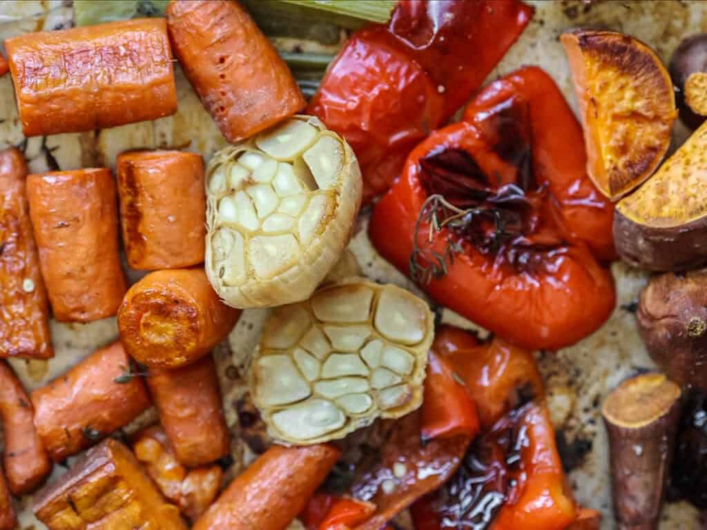 Gochujang and Roasted Carrot Soup - SPICY AND EASY. 10 A close-up of roasted vegetables, including sliced carrots, red bell peppers, and garlic bulbs. The vegetables are caramelized and slightly charred, showcasing a rustic and appetizing presentation.