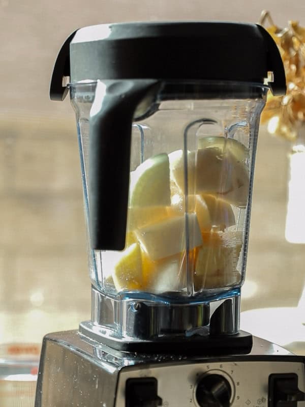 Mom's Easy White Kimchi (Baek-Kimchi) Recipe (백김치). 22 A blender filled with chopped apples, placed on a kitchen counter. Sunlight streams from a nearby window, casting shadows and highlighting the fresh fruit inside the transparent blender jar.