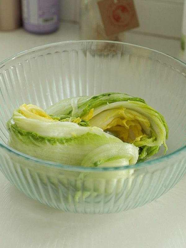 Mom's Easy White Kimchi (Baek-Kimchi) Recipe (백김치). 5 A glass bowl containing a halved head of napa cabbage with light green and yellow leaves, placed on a kitchen countertop.
