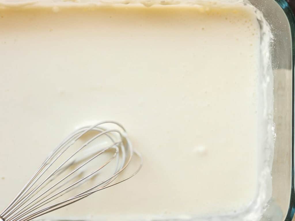The BEST Vegan Lasagna Recipe - Easy and Delicious. 19 A whisk stirring a tempura batter in a glass baking dish, suggesting a mixture being prepared. The liquid is smooth and evenly distributed across the dish.