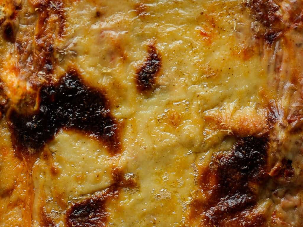 The BEST Vegan Lasagna Recipe - Easy and Delicious. 42 Close-up of a golden-brown, baked cheesy surface with some dark, crispy spots. The texture appears melted and slightly bubbly, suggesting a dish like lasagna or a casserole.