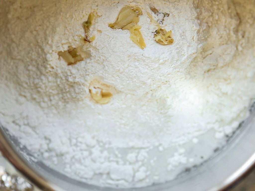 Perfect Roasted Garlic Vegan Dinner Rolls Recipe. 13 A metal mixing bowl filled with white flour and roasted garlic. The ingredients are ready to be mixed for baking.