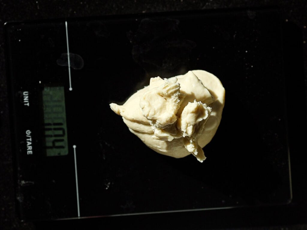 Perfect Roasted Garlic Vegan Dinner Rolls Recipe. 25 Dough ball resting on a digital kitchen scale displaying weight in a dimly lit setting.
