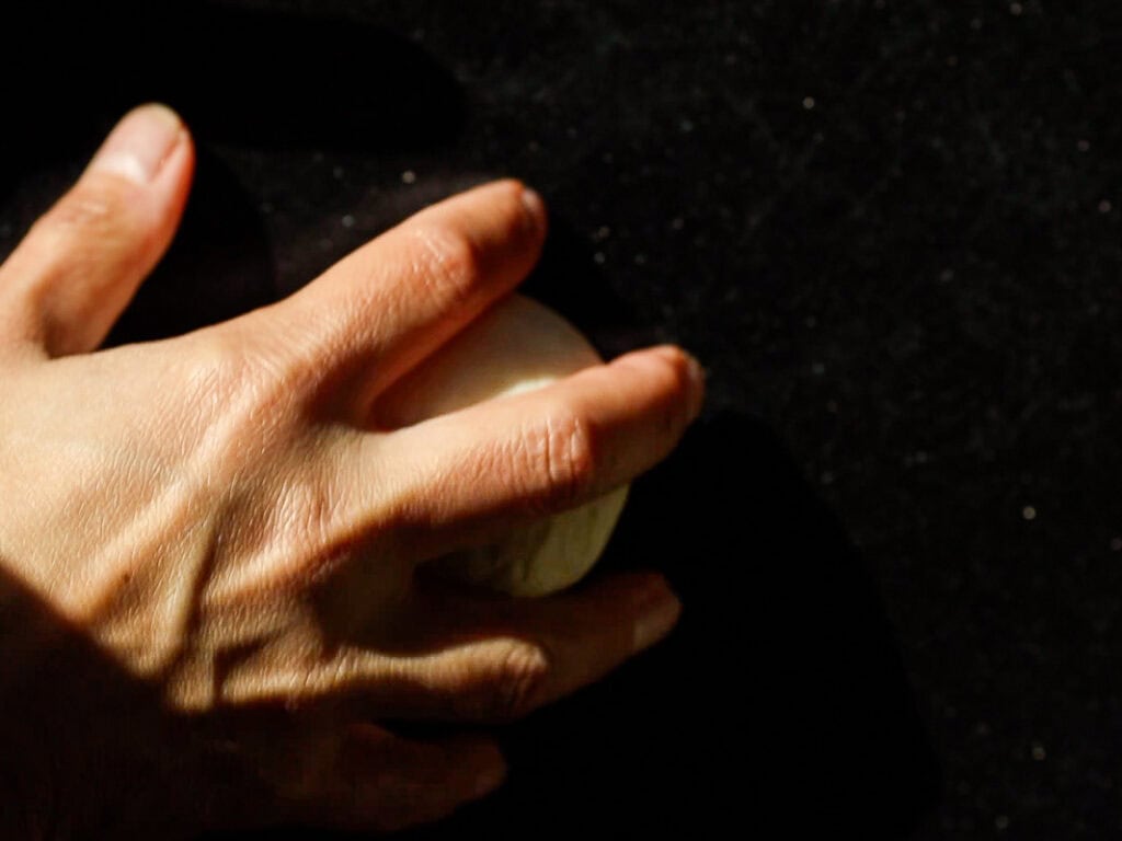 Perfect Roasted Garlic Vegan Dinner Rolls Recipe. 28 A hand kneading a small ball of dough on a dark surface, with sunlight casting shadows on the fingers.