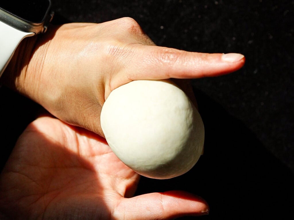 Perfect Roasted Garlic Vegan Dinner Rolls Recipe. 27 A person wearing a white smartwatch molds a ball of dough in their hands against a dark background.
