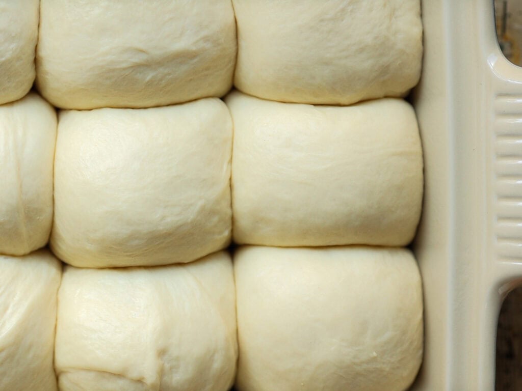 Perfect Roasted Garlic Vegan Dinner Rolls Recipe. 31 Close-up of uncooked, fluffy dough rolls neatly arranged in a baking dish, ready for baking.