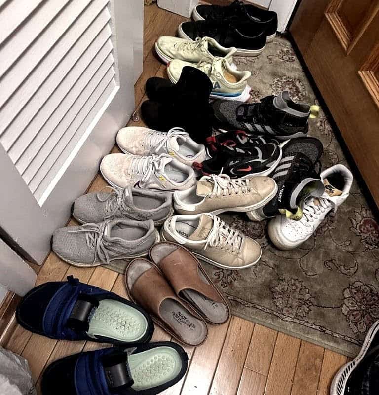 Friend Breakups 2 A cluttered pile of various shoes, including sneakers, sandals, and slippers, is scattered on a patterned rug near a wooden door. The scene hints at a family gathering for Thanksgiving.