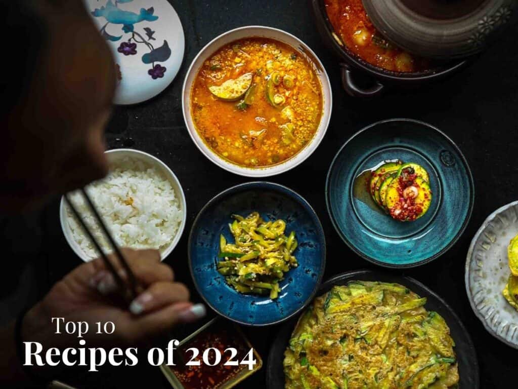 A Note on New Year's Resolutions 2 A person eating with chopsticks at a table featuring various dishes, including rice, soup, kimchi, and a vegetable pancake. The image is titled Top 10 Recipes of 2024, aligning perfectly with New Years Resolutions to explore diverse flavors and healthy eating habits.