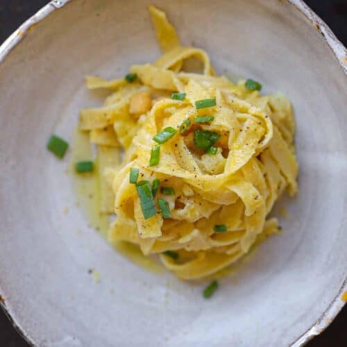 5-Ingredient Easy Chickpea Pasta Recipe (Pasta e Ceci). 24 A bowl featuring chickpea pasta recipe topped with a creamy sauce and garnished with chopped green herbs, set against a dark background. The dish is served in a rustic, textured bowl.