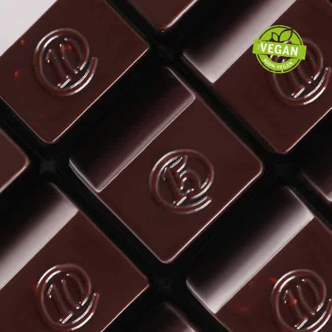 The Korean Vegan's 2025 VEGAN Holiday Gift GUIDE. 48 Close-up of dark chocolate squares with embossed logos, arranged neatly. In the top right corner, a green Vegan label proudly certifies them as part of the 2024 Korean Vegan Holiday Gift Guide.