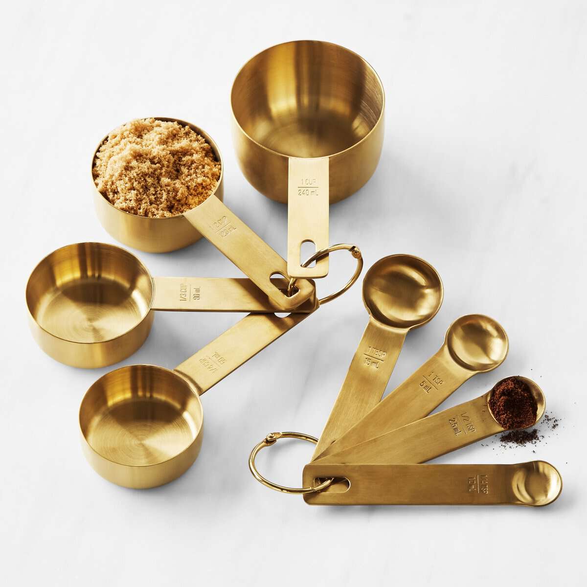 The Korean Vegan's 2025 VEGAN Holiday Gift GUIDE. 8 A perfect holiday gift, this set of gold measuring cups and spoons displayed on a white surface is ideal for any kitchen. Each cup filled with brown sugar and each spoon sprinkled with spices, offers precise measurement markings—an essential guide for any culinary adventure.