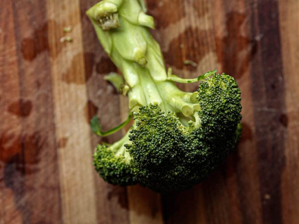 Creamy Broccoli Soup with Dumplings - delicious and Gluten-Free! 3 Fresh broccoli on a wooden cutting board, showing its stalk and florets in vivid green hues.
