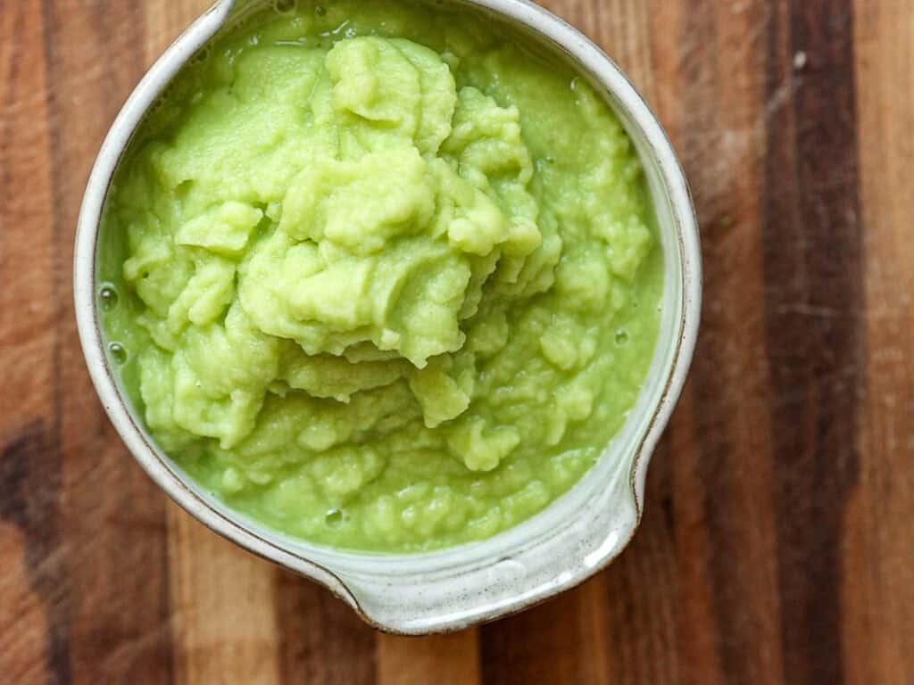 Creamy Broccoli Soup with Dumplings - delicious and Gluten-Free! 6 A small, white ceramic bowl filled with creamy broccoli puree on a wooden surface. The avocado has a smooth, green texture and looks fresh and appetizing.