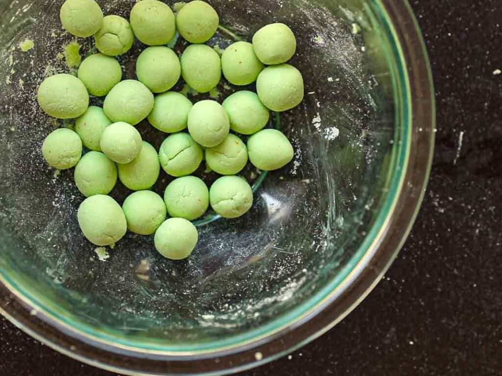 Creamy Broccoli Soup with Dumplings - delicious and Gluten-Free! 11 A glass bowl with small green dough balls on a dark countertop. Some flour residue is visible inside the bowl.