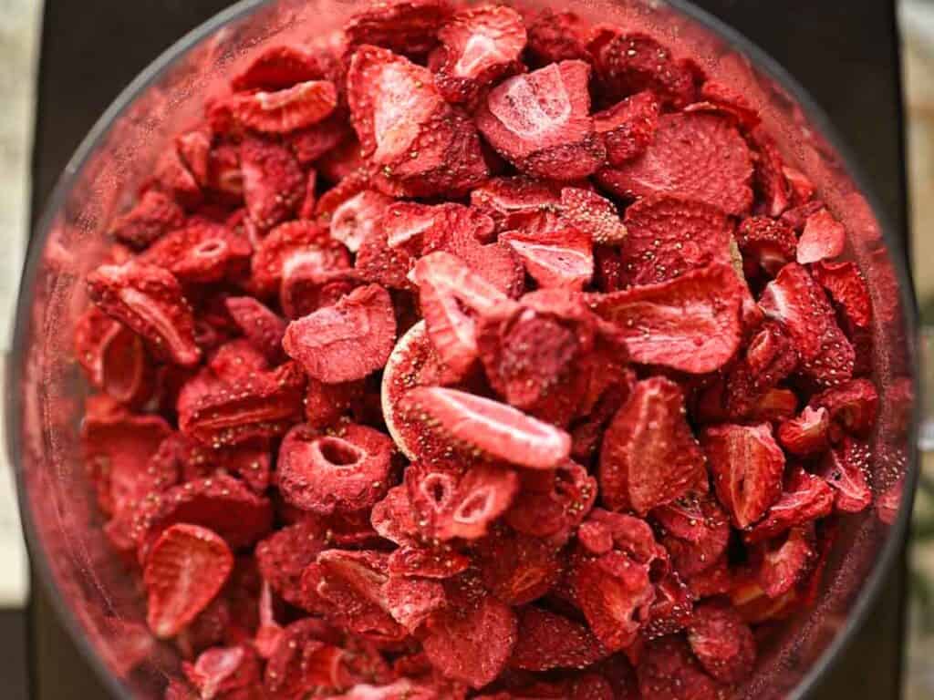Stunning Pink Vegan Strawberry Cake (Fresh berries). 13 A close-up of a bowl filled with freeze-dried strawberry slices. The strawberries are vibrant red with visible seeds and varied textures, suggesting a crunchy texture.