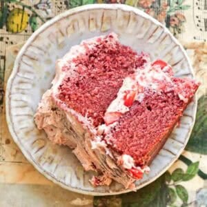 Stunning Pink Vegan Strawberry Cake (Fresh berries). 38 A slice of vegan strawberry came with vegan buttercream frosting and strawberry pieces on a decorative plate. The plate rests on a table with a floral and musical notes design.