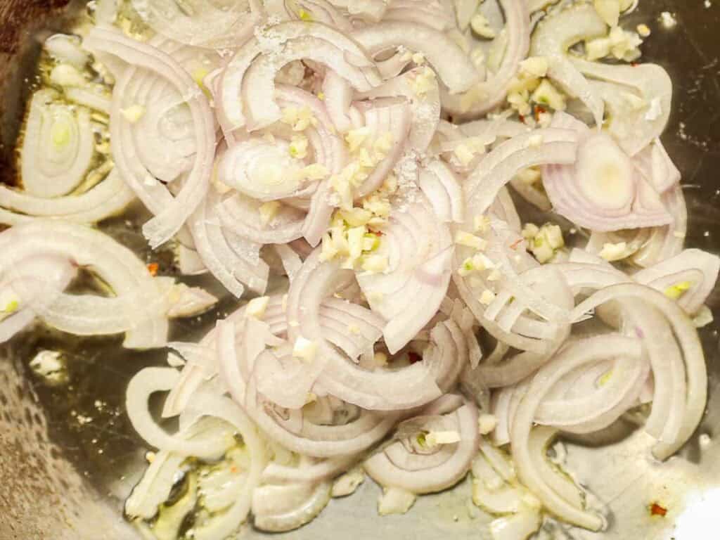 30-Minute Creamy Gochujang Vodka Pasta - Delicious & Dairy-FREE. 13 Close-up of thinly sliced shallots and minced garlic sizzling in a pan, creating a base for cooking. The ingredients are lightly browning and releasing a savory aroma.