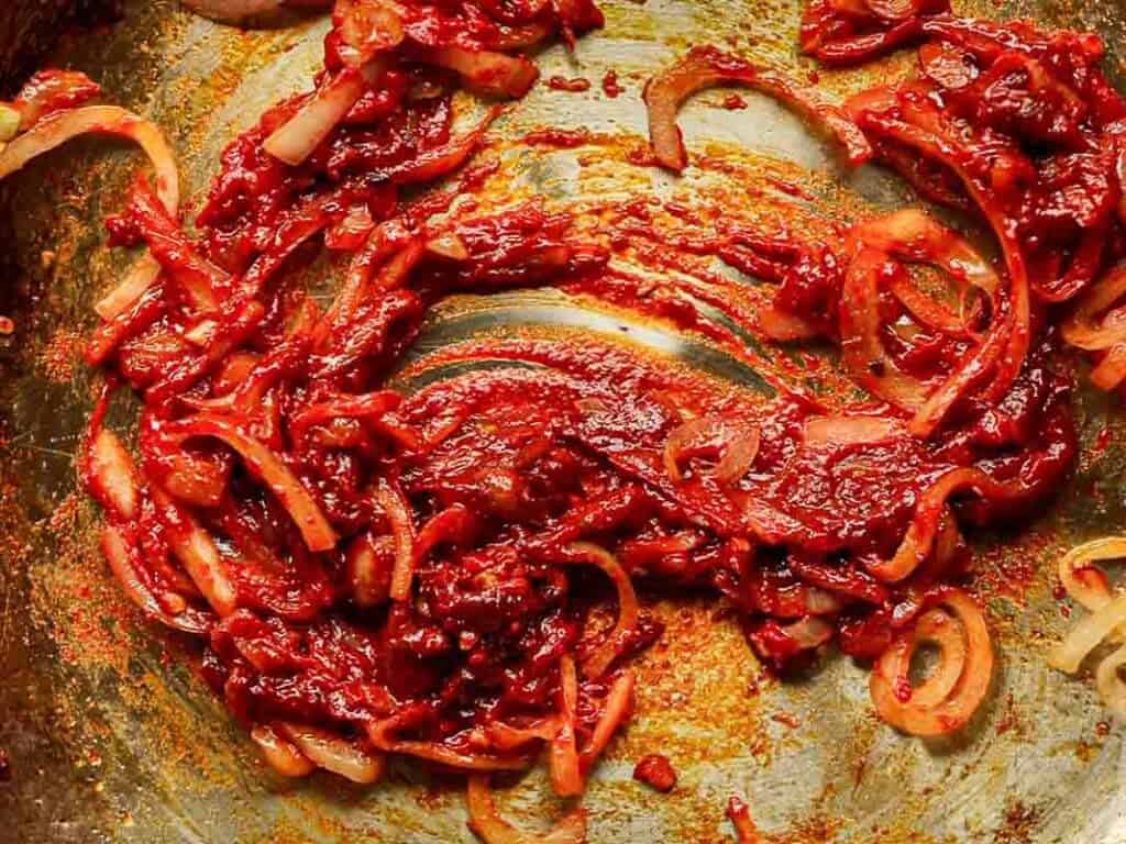 30-Minute Creamy Gochujang Vodka Pasta - Delicious & Dairy-FREE. 16 A close-up of vibrant red sauce spread over a textured surface, mixed with sliced shallots. The sauce appears thick and rich, with visible spices and a slightly glossy texture.