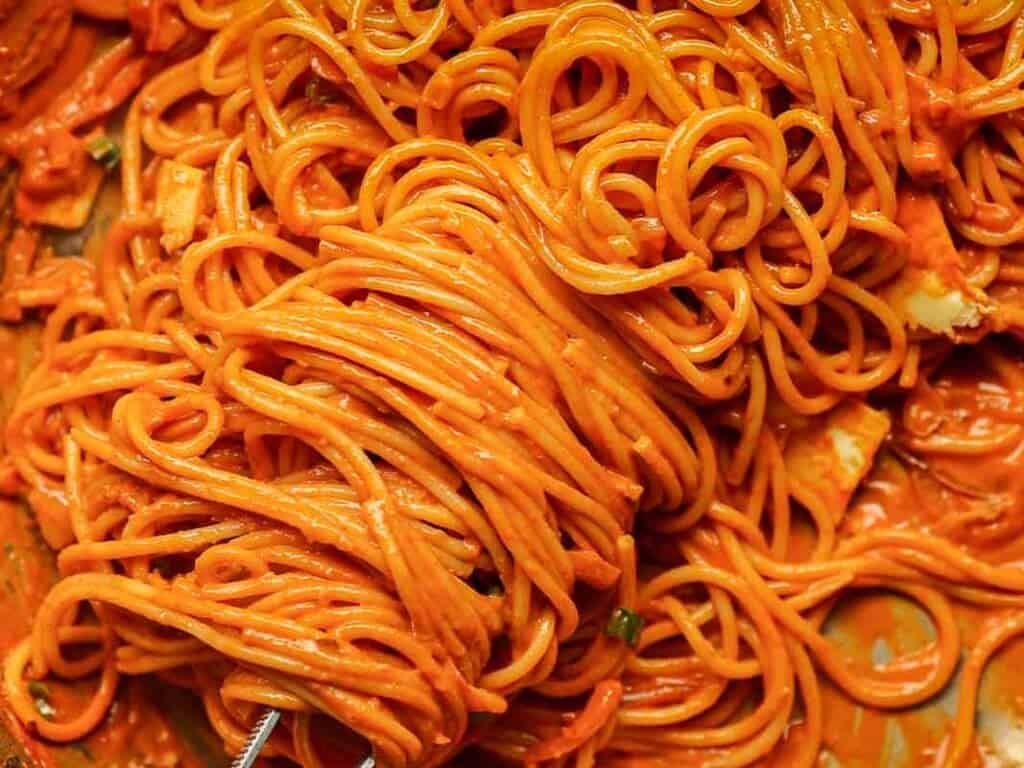 30-Minute Creamy Gochujang Vodka Pasta - Delicious & Dairy-FREE. 3 A close-up of spaghetti covered in a thick, red sauce. The noodles are tangled and saturated with the vibrant sauce, giving the dish a rich appearance. Small bits of herbs and spices are visible throughout.