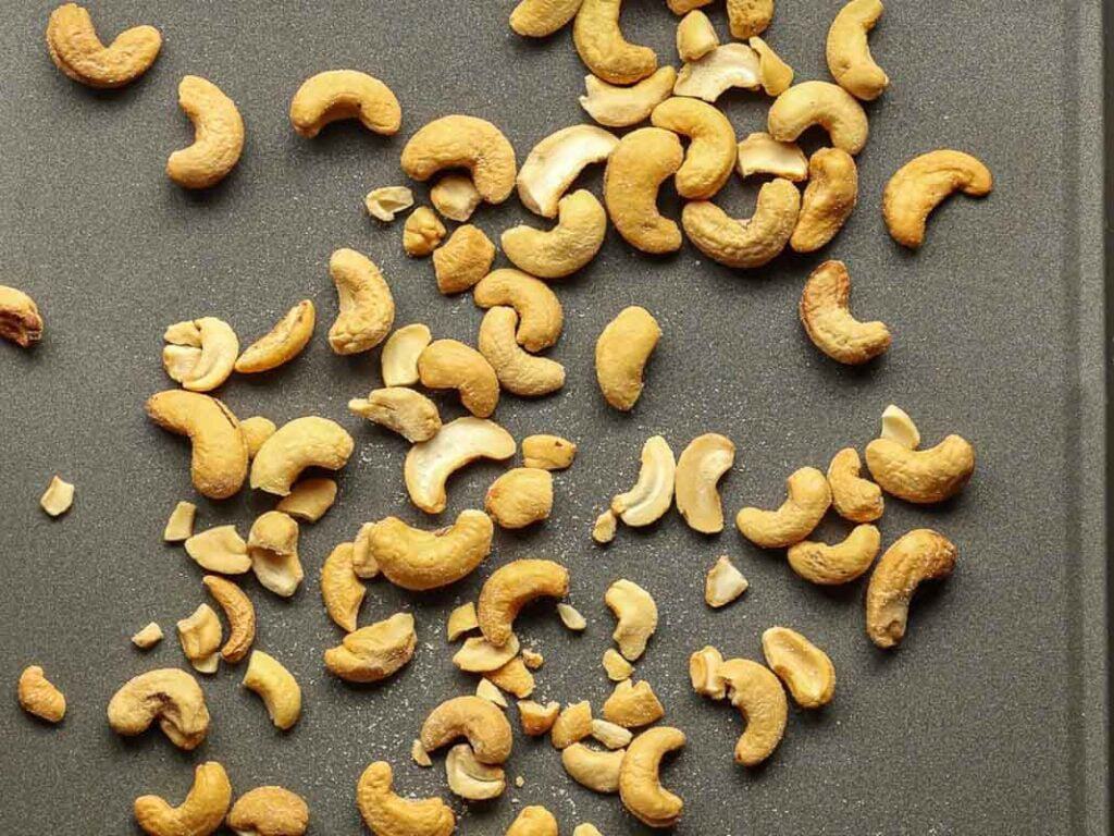 Delicious and Easy Vegan Cashew Nut Stir Fry Recipe. 5 Scattered roasted cashews on a flat grey surface, showcasing various whole nuts and some broken pieces.