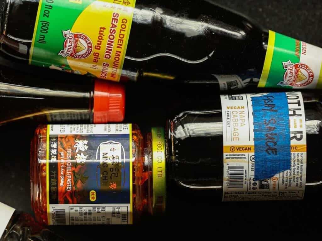 Delicious and Easy Vegan Cashew Nut Stir Fry Recipe. 7 A close-up of various Asian condiments including a bottle of Golden Mountain seasoning sauce, a jar of chili paste, and a bottle labeled fishy sauce. The chili paste jar has a red lid and Asian characters on the label.