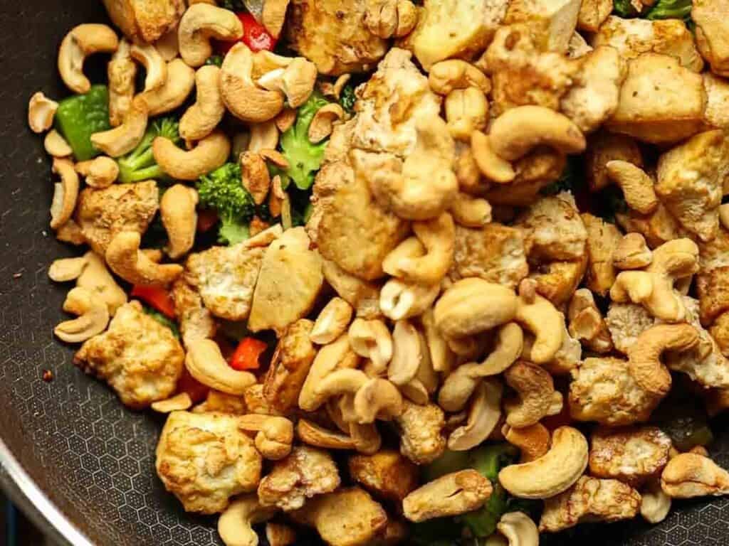Delicious and Easy Vegan Cashew Nut Stir Fry Recipe. 23 A pan filled with a colorful stir-fry featuring chunks of tofu, broccoli, red bell pepper, and a generous amount of cashew nuts. The ingredients are lightly sautéed, giving the dish a vibrant and appetizing appearance.
