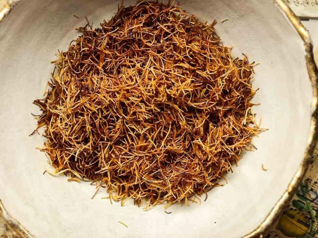 A close-up of a ceramic bowl filled with toasted kataifi strands. The reddish-orange threads are loosely arranged, showcasing their delicate and thin texture against the neutral color of the bowl.