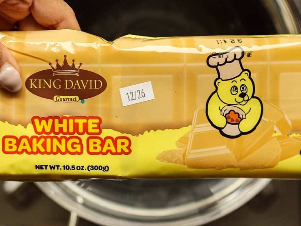 Viral Dubai Chocolate Bar with Strawberry Filling (Vegan). 3 A person holds a package of King David Gourmet White Baking Bar. The packaging features a cartoon bear in a chefs hat, holding a heart-shaped item. The net weight is 10.5 oz (300g). The package also has a small white sticker with the numbers 12/26.