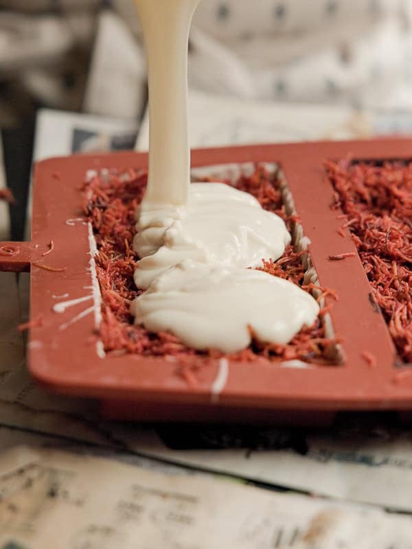 Pouring creamy liquid into silicone molds filled with strawberry kataifi, set on a surface covered with newspapers.