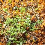 10+ Delicious and Easy Recipes Using Kimchi Today! 12 Close-up of a vibrant dish featuring vegan kimchi fried rice mixed with chopped vegetables. The dish is topped with a generous amount of sliced green onions and sprinkled with sesame seeds, giving it a colorful and textured appearance.
