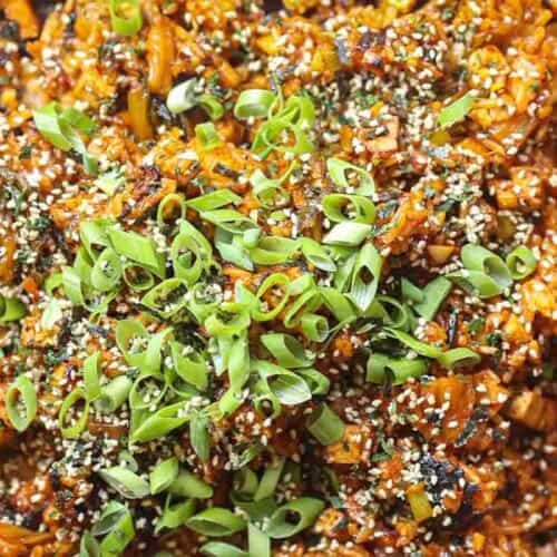 Healthy & Easy Korean Vegan Kimchi Fried Rice Recipe. 34 Close-up of a vibrant dish featuring vegan kimchi fried rice mixed with chopped vegetables. The dish is topped with a generous amount of sliced green onions and sprinkled with sesame seeds, giving it a colorful and textured appearance.