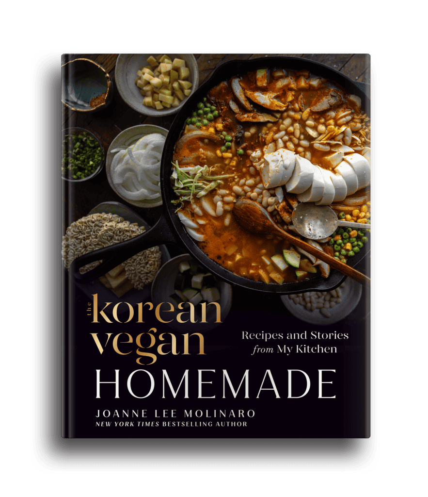 Home 14 The cover of The Korean Vegan Cookbook by Joanne Lee Molinaro showcases a homemade bowl of stew with sliced tofu, mushrooms, green onions, and rice cakes. Surrounding the bowl are an array of ingredients like beans and spices. The text reads Recipes and Stories from My Kitchen.